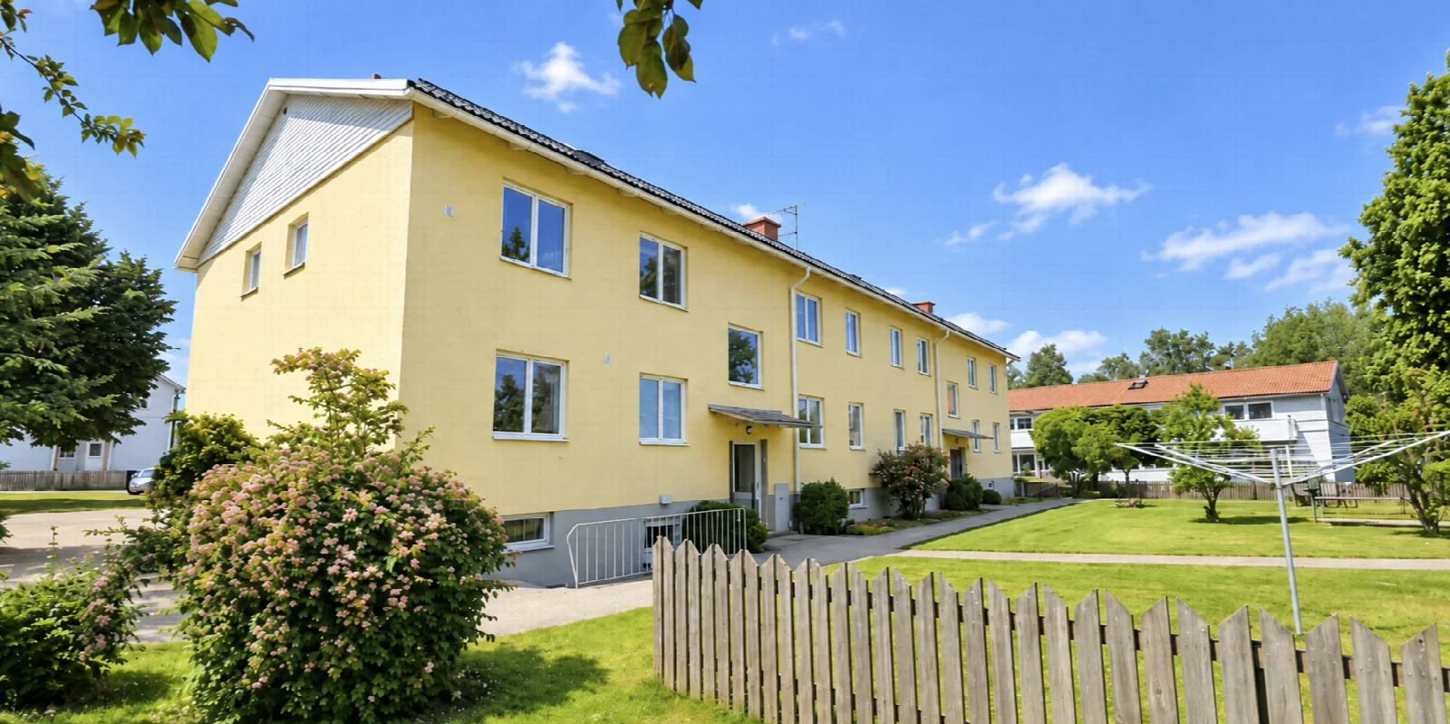 Gult bostadshus med grön gård på Mjölbyvägen 21 i Sya